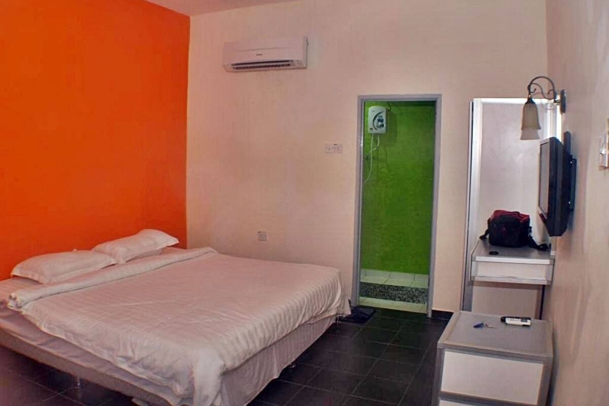 A hotel room with a bed, a small table, a mirror, and a green door.