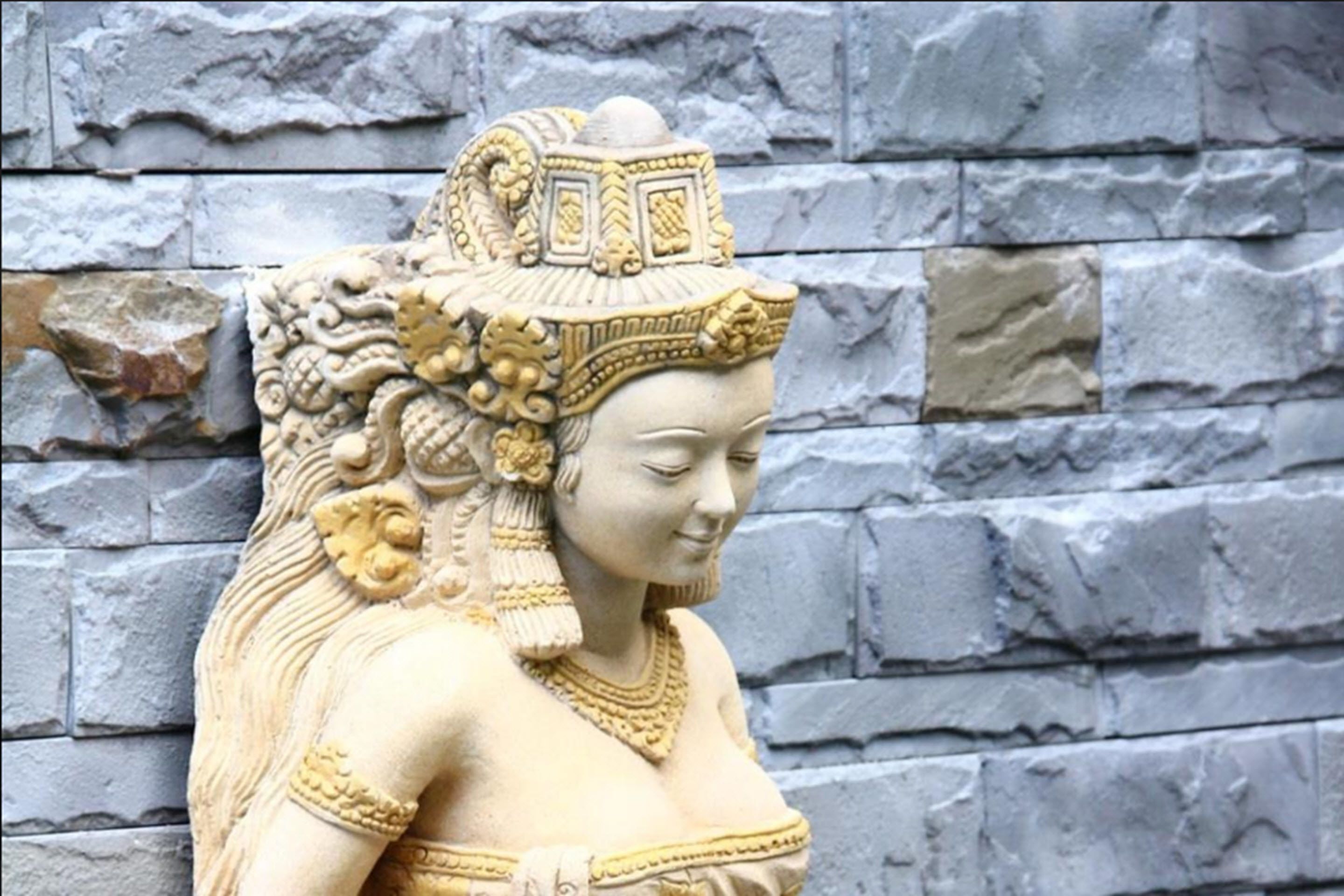 Eine Steinsäule mit einer gemeißelten Statue einer Person mit aufwendiger Kopfbedeckung.