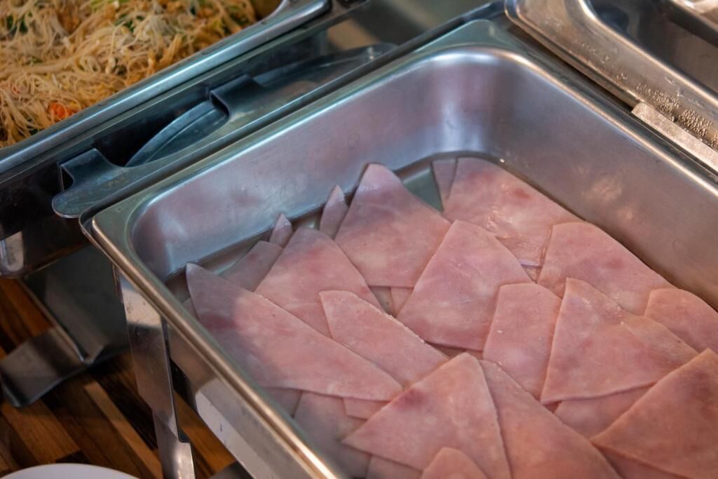 En buffet med en rustfri serveringsbakke med pænt anrettede, trekantede skiver af skinke.