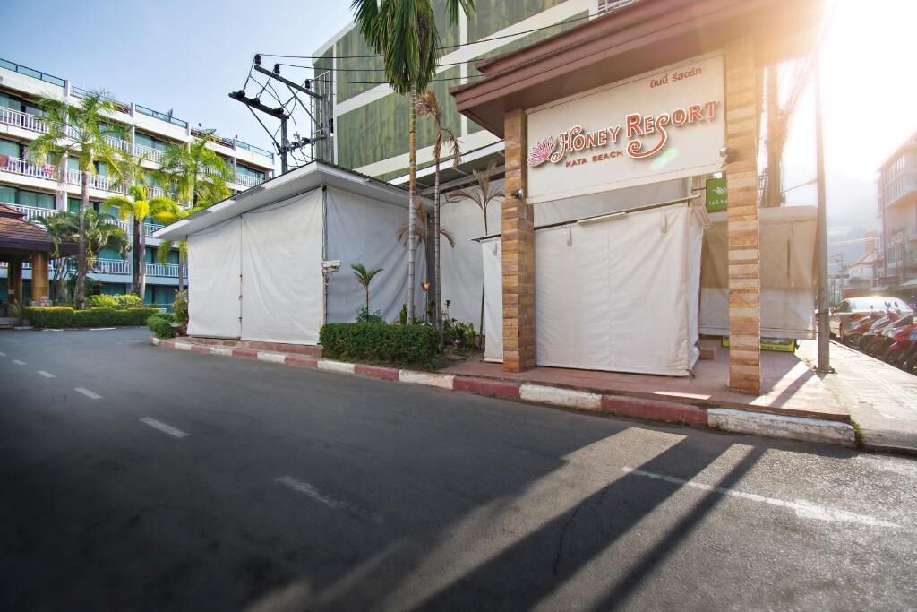 Een hotel genaamd "Honey Resort" met een overdekte ingang en uitzicht op een meer verdiepingen tellend gebouw op de achtergrond.