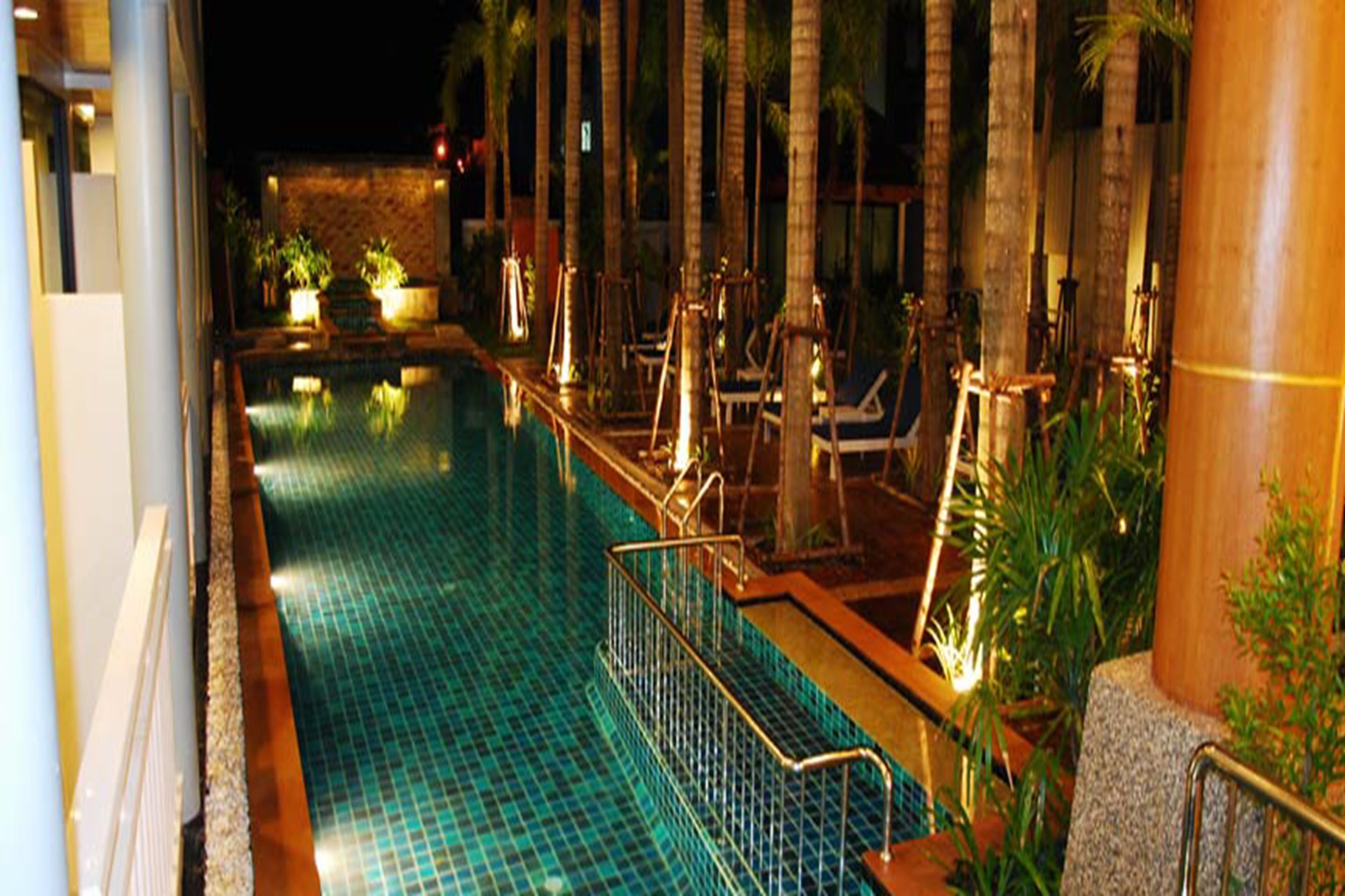 Ein Pool mit gefliestem Boden, umgeben von Liegestühlen und Palmen, typisch für eine luxuriöse Hotelanlage.