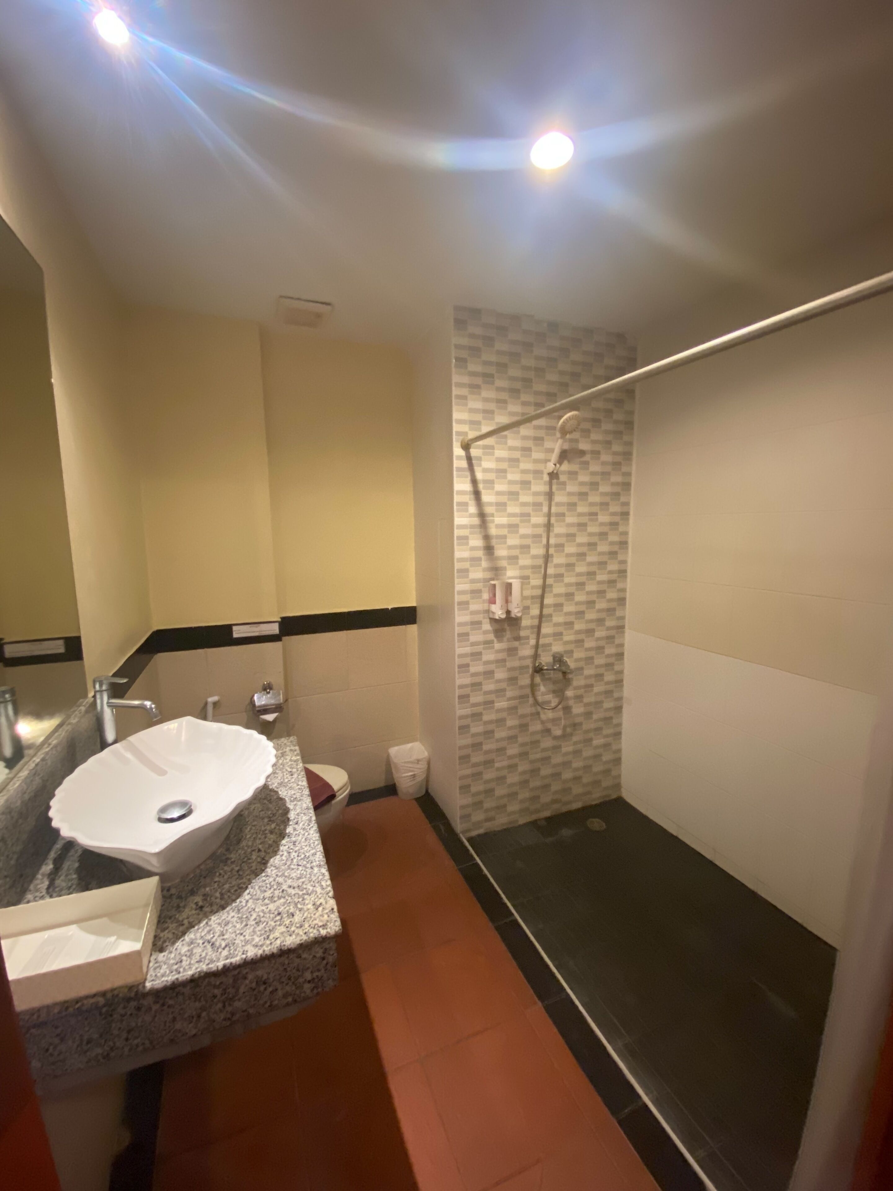 A bathroom with a granite countertop, a white sink, a shower with a glass door, and a tiled wall.