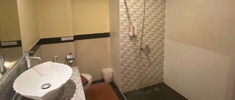 A bathroom with a granite countertop, a white sink, a shower with a glass door, and a tiled wall.