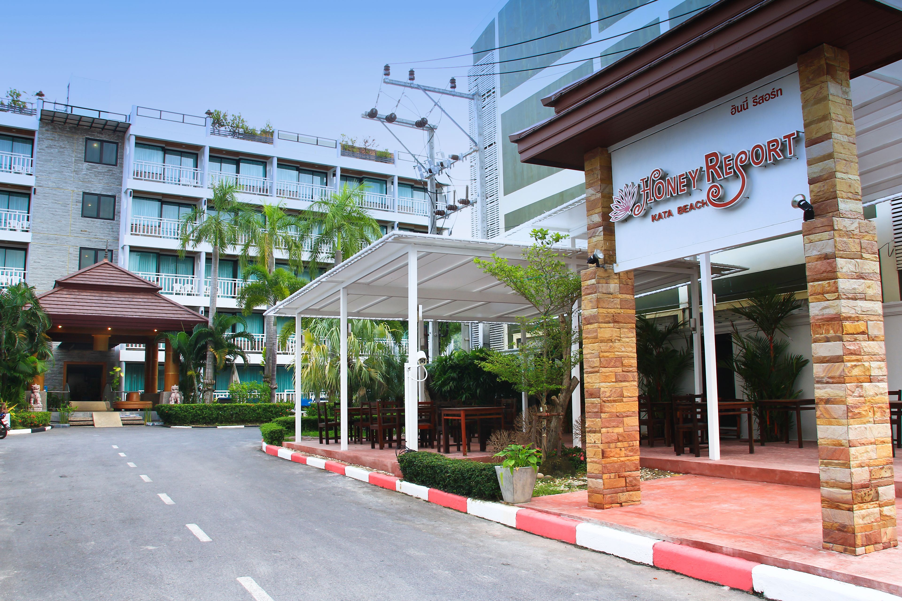 A hotel entrance with a covered outdoor seating area, a clear sky, and a multi-story building in the background.