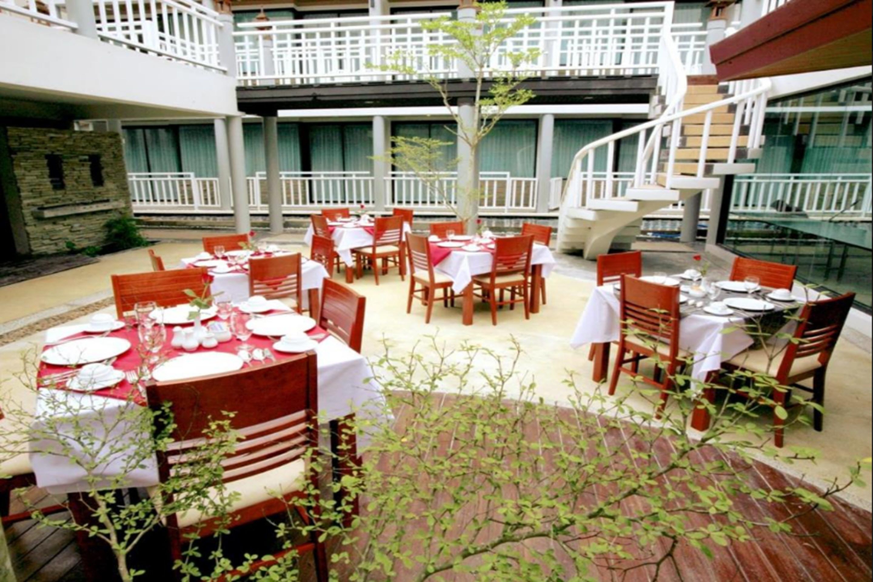 Un área de comedor al aire libre con mesas y sillas, una escalera y vistas al interior del edificio.