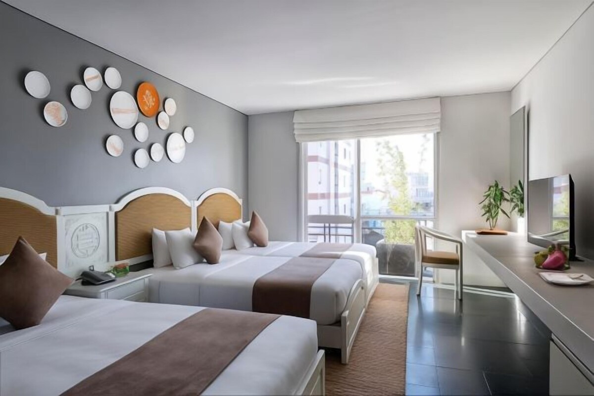 Quarto de hotel com duas camas, uma janela ampla com vista, uma televisão de tela plana e uma pequena mesa com uma planta.