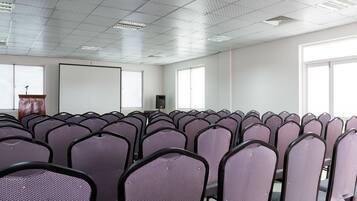 A conference room with rows of chairs, a podium, and a projector screen.