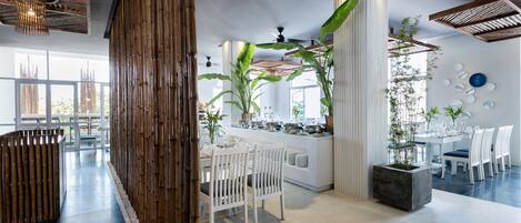A modern dining area with white furniture, bamboo accents, and large windows.