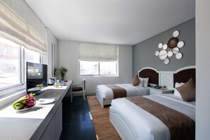 A hotel room with two beds, a desk with a TV, a window with a view of buildings, and a wall decoration. - Alba Spa Hotel (Hue)