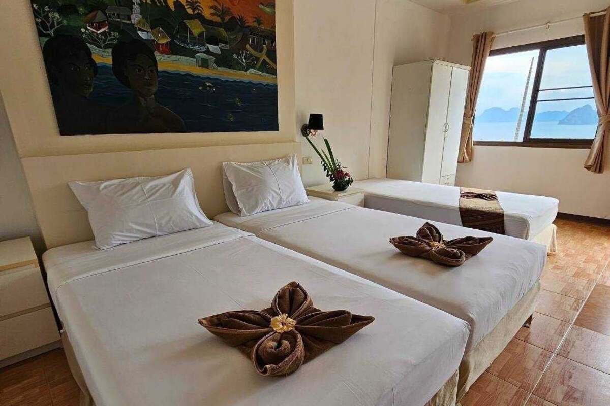 Habitación de hotel con dos camas, un cuadro en la pared, una ventana con vistas y una planta en la mesita de noche.
