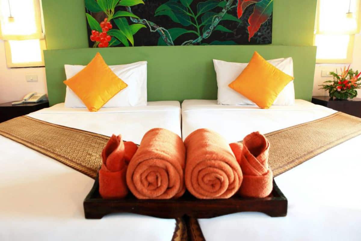 Une chambre d’hôtel avec deux lits, des têtes de lit vertes, du linge de lit blanc et des oreillers orange.
