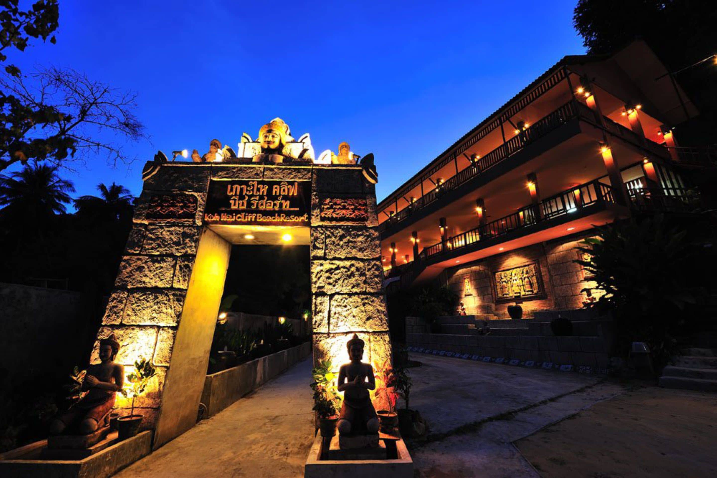 Un arco de piedra con una estatua de Buda, que conduce a un edificio con varios balcones y un letrero que dice "Koh Musai Cliff Beach Resort".