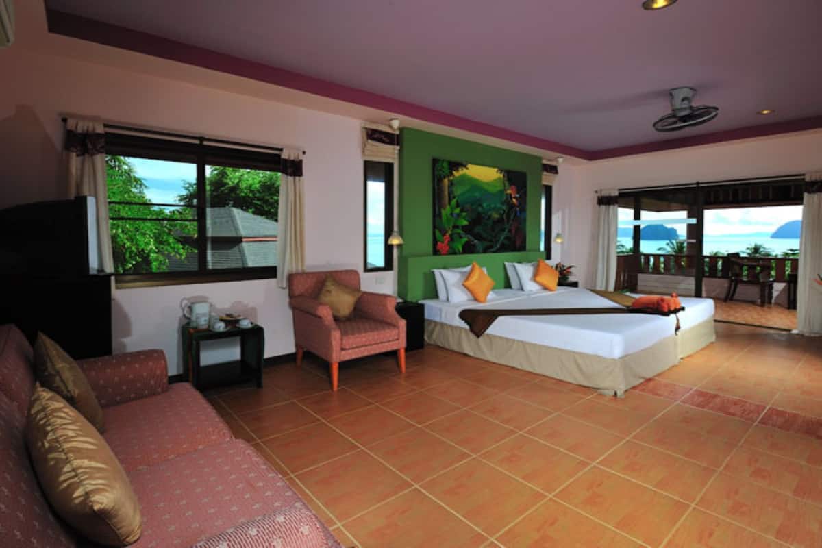 Une chambre d’hôtel avec un lit, une chaise, un canapé, un tableau au mur et une vue sur la mer.