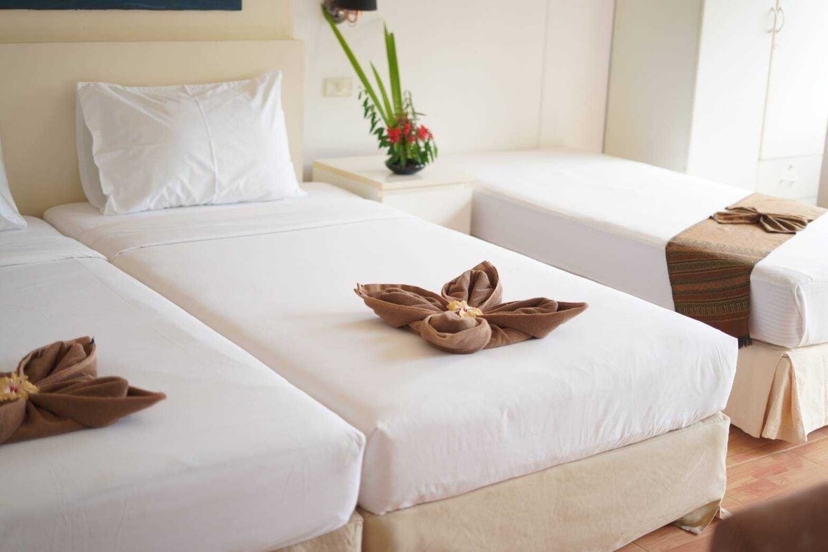 Habitación de hotel con dos camas, ropa blanca y toallas marrones dispuestas en forma de flor sobre las camas.