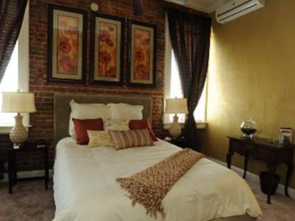 Ein Hotelzimmer mit Backsteinwand, einem großen Bett mit vielen Kissen, einem Nachttisch mit Lampe und einem Bilderrahmen an der Wand.