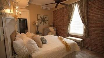 A bedroom with a bed, a ceiling fan, a brick wall, and a window with curtains.