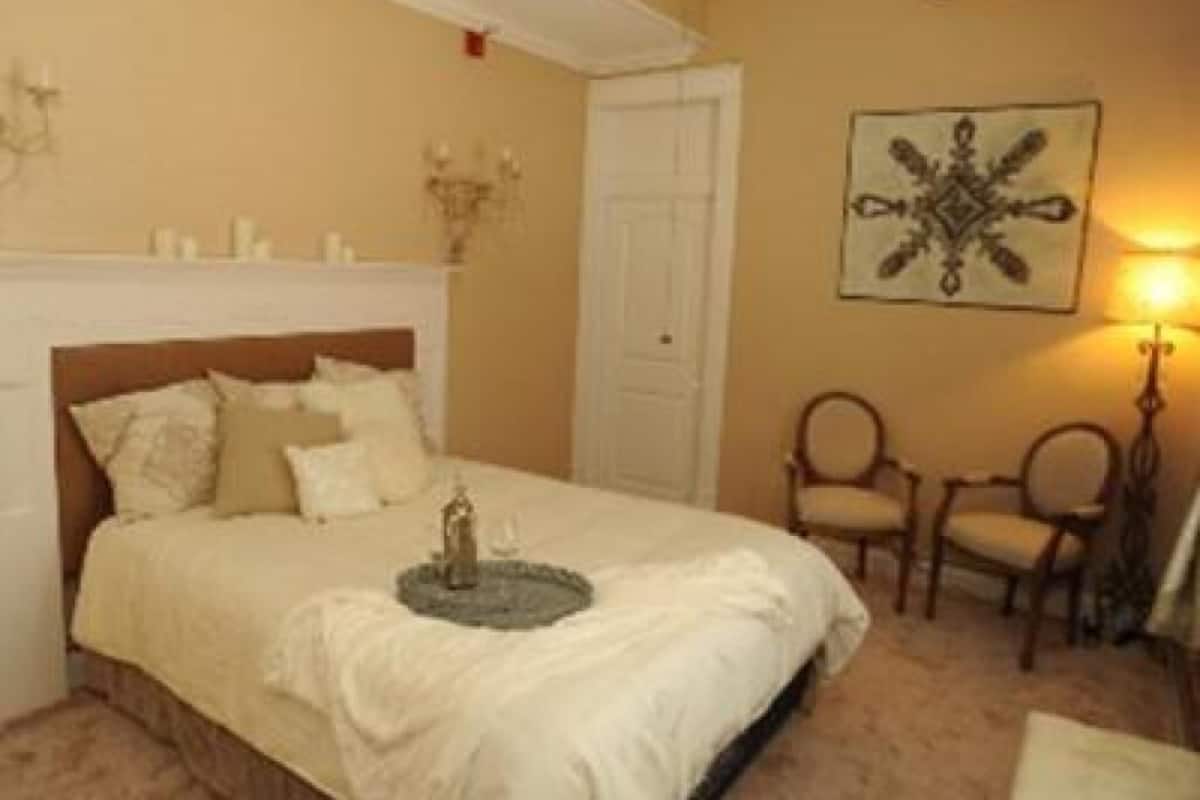 A bedroom with a bed, two chairs, a wall-mounted artwork, and a door.