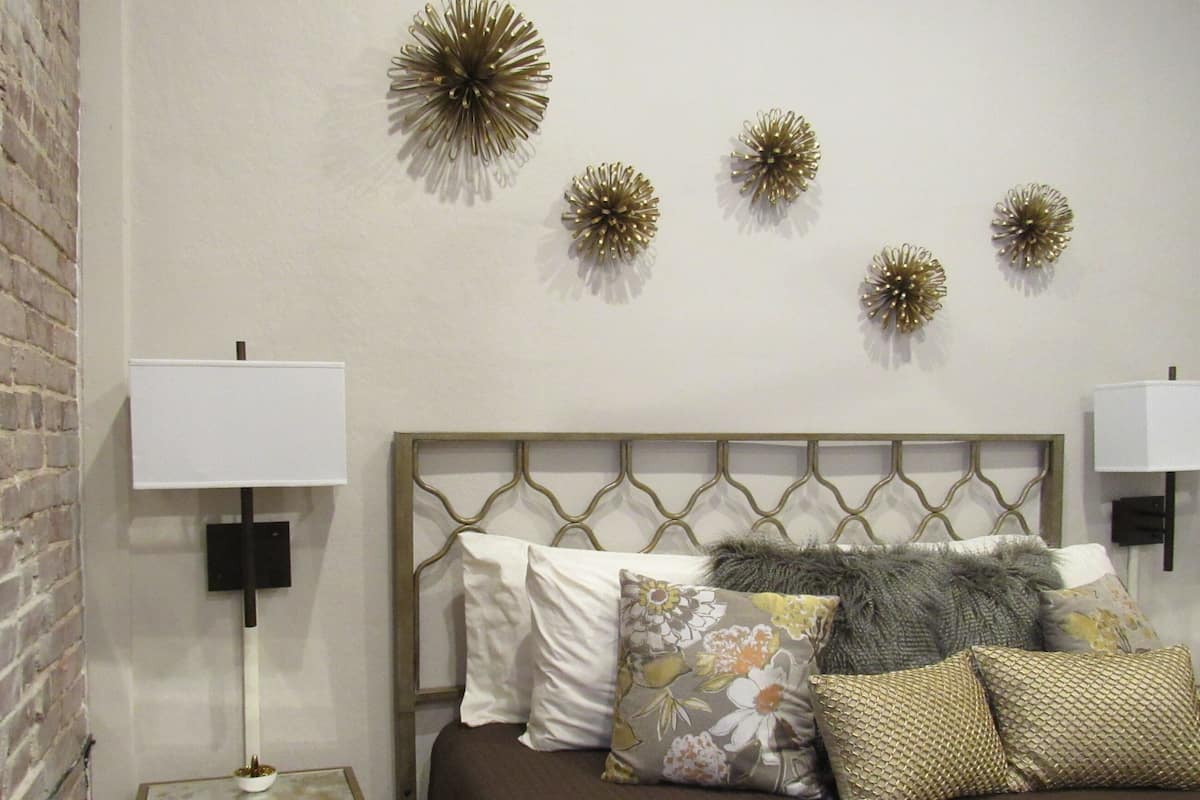 A bedroom with a brick wall, a bed with multiple pillows, and decorative wall art.