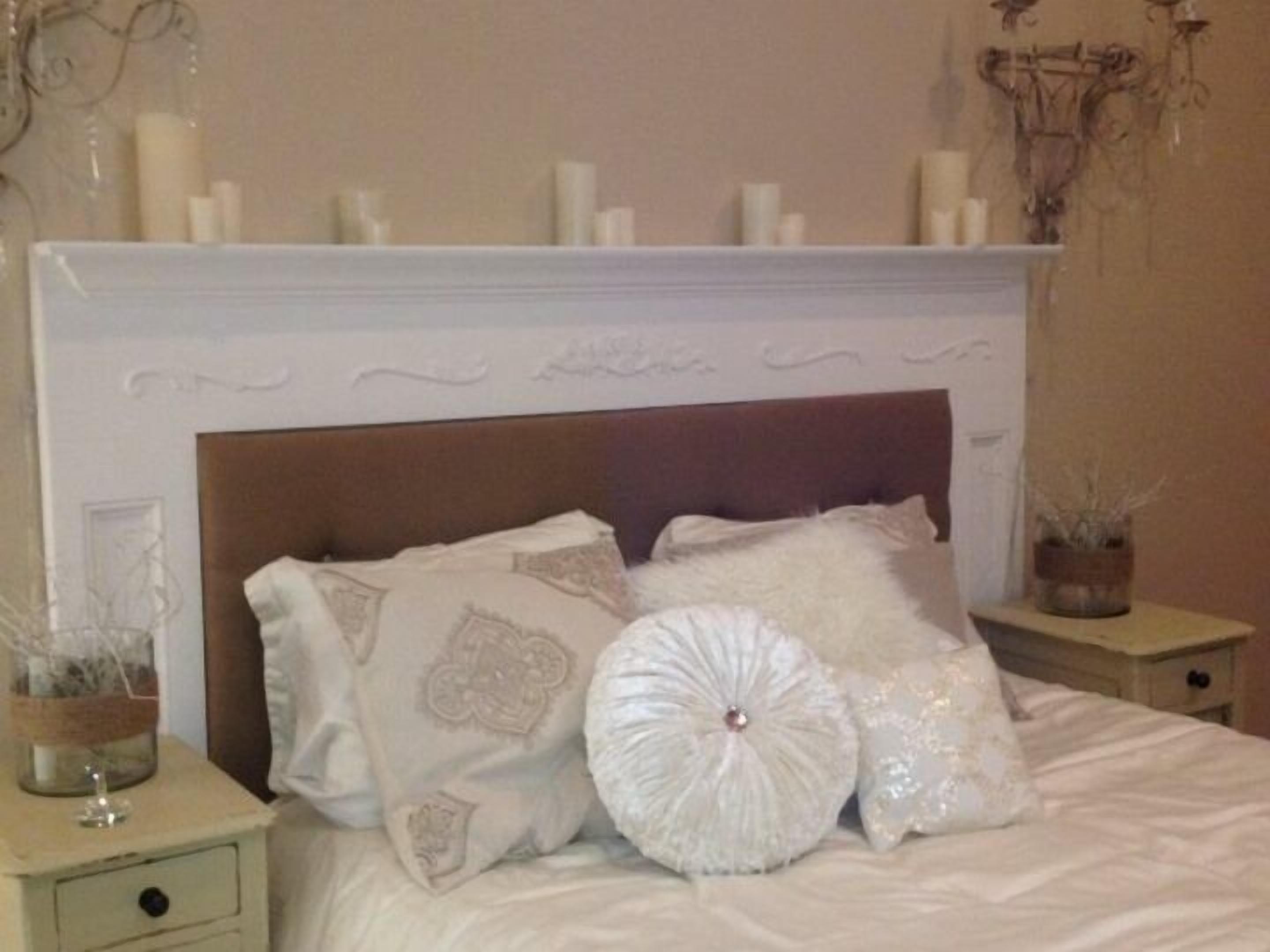 A bedroom with a white fireplace, a wooden headboard, and decorative pillows.