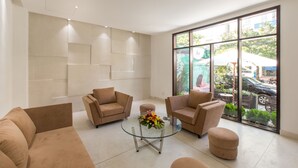 A modern lobby with beige sofas, a glass coffee table with a floral centerpiece, and large windows offering a view of the outdoors. - Alba Hotel (Hue)