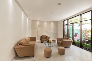 A modern living room with beige sofas, a glass coffee table, and a large window with a view of the outdoors. - Alba Hotel (Hue)