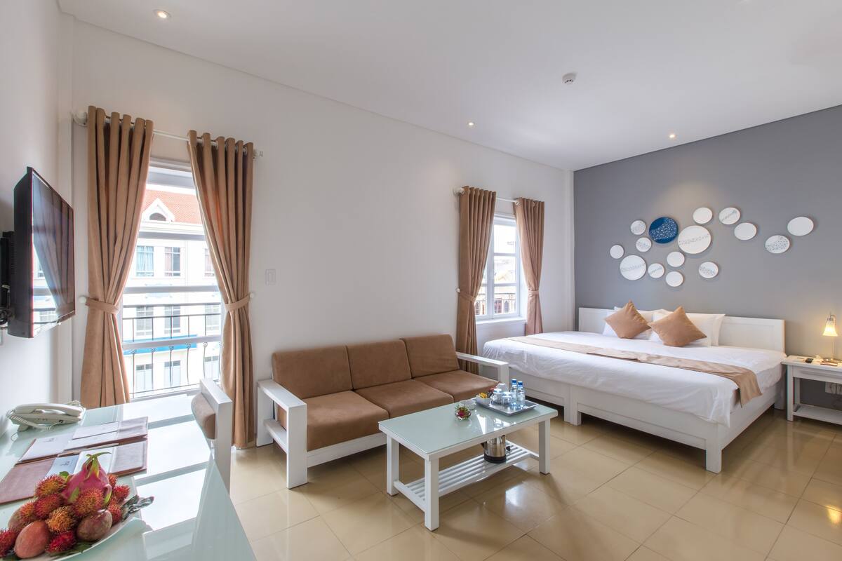 A modern hotel room with a bed, sofa, and a dining table.