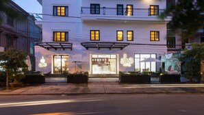 A building with a café and a hotel entrance, featuring a modern design with large windows and outdoor seating. - Alba Hotel (Hue)