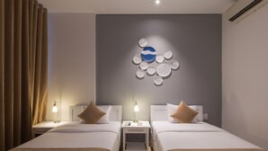 A hotel room with two beds, a nightstand with a lamp, a wall art piece, and a window with curtains. - Alba Hotel (Hue)