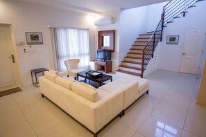 A modern living room with a sofa, a coffee table, a TV, and a staircase. - Tumon Bel-Air Serviced Residence (Tamuning)
