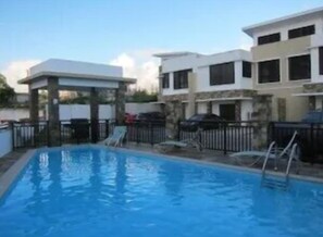 A swimming pool with a slide, surrounded by a fenced area and a building with multiple windows. - Tumon Bel-Air Serviced Residence (Tamuning)
