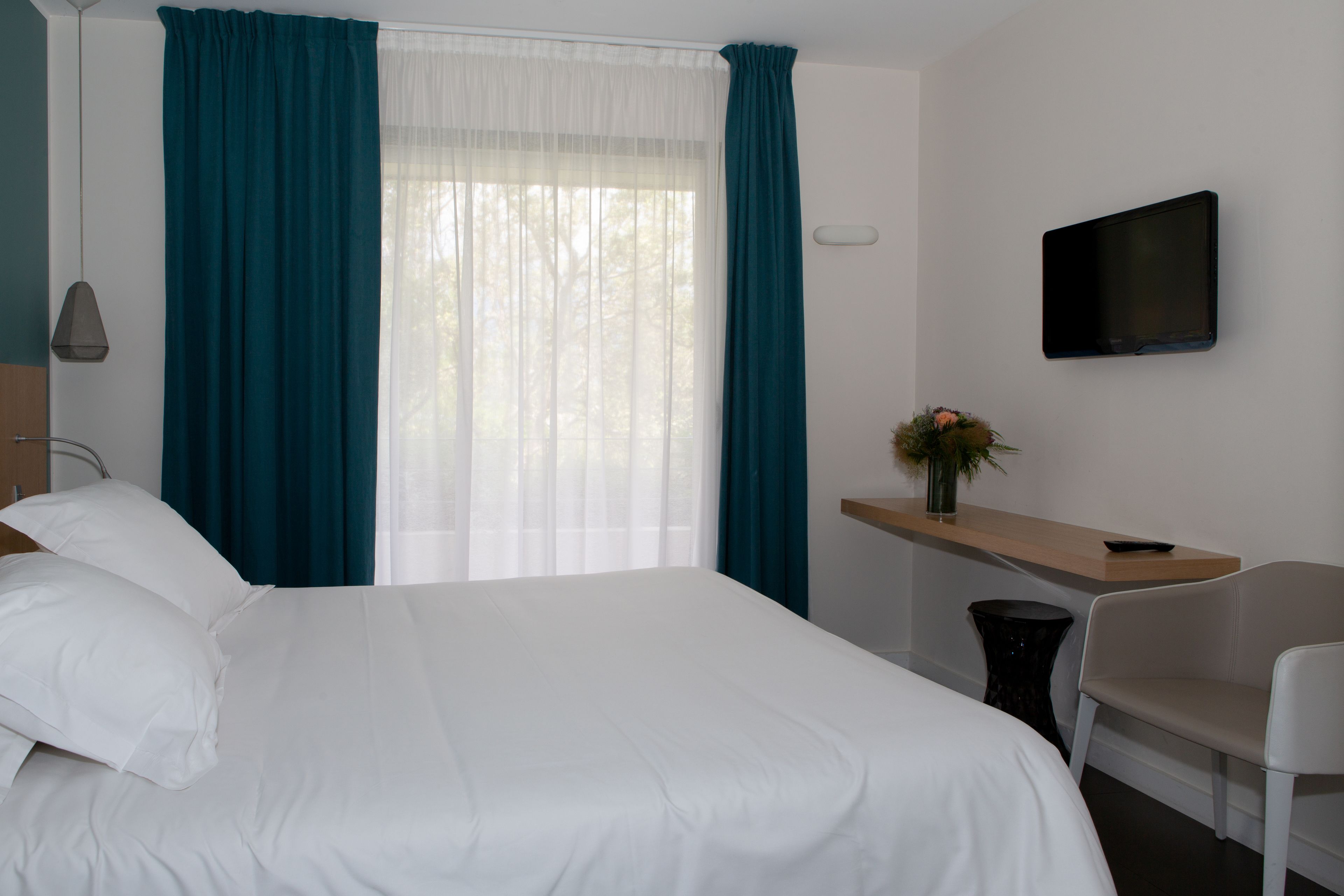A hotel room with a bed, a desk, a chair, a TV, and a window with curtains.