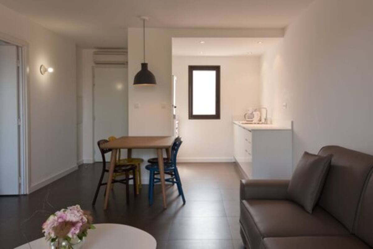 Ein modernes Wohnzimmer mit einem braunen Sofa, einem Esstisch mit Stühlen und einer Küche im Hintergrund.