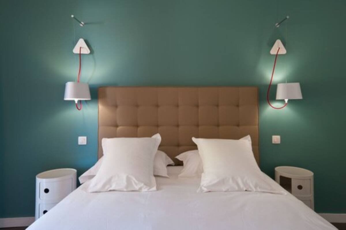 Ein Schlafzimmer mit einem gepolsterten Kopfteil, weißer Bettwäsche, zwei Nachttischen und Wandlampen.
