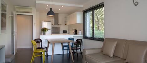 Een moderne woonkamer met een beige bank, een witte salontafel, en een eethoek met een houten tafel en stoelen.