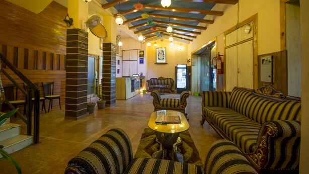 Um hall amplo com teto alto, vigas de madeira, lareira, sofá, mesa de centro e uma escadaria.