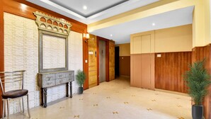 Um hall moderno com parede de pedra, balcão de recepção em madeira, uma cadeira, plantas em vasos e piso ladrilhado.