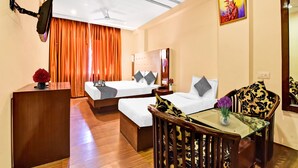 Quarto de hotel com duas camas, uma escrivaninha, uma cadeira, um ventilador de teto e um quadro na parede.