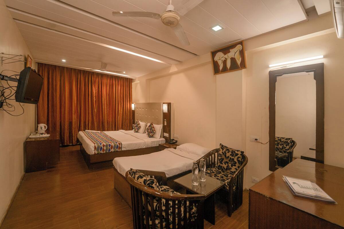 A hotel room with two beds, a desk with a chair, a mirror, and a ceiling fan.
