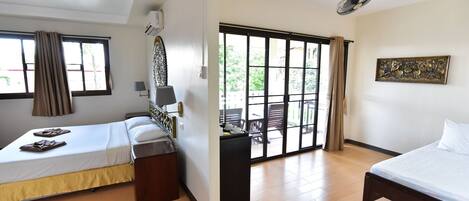 Habitación de hotel con dos camas, un escritorio, una silla, una ventana con cortinas, una puerta que da a un espacio exterior y un ventilador de techo.
