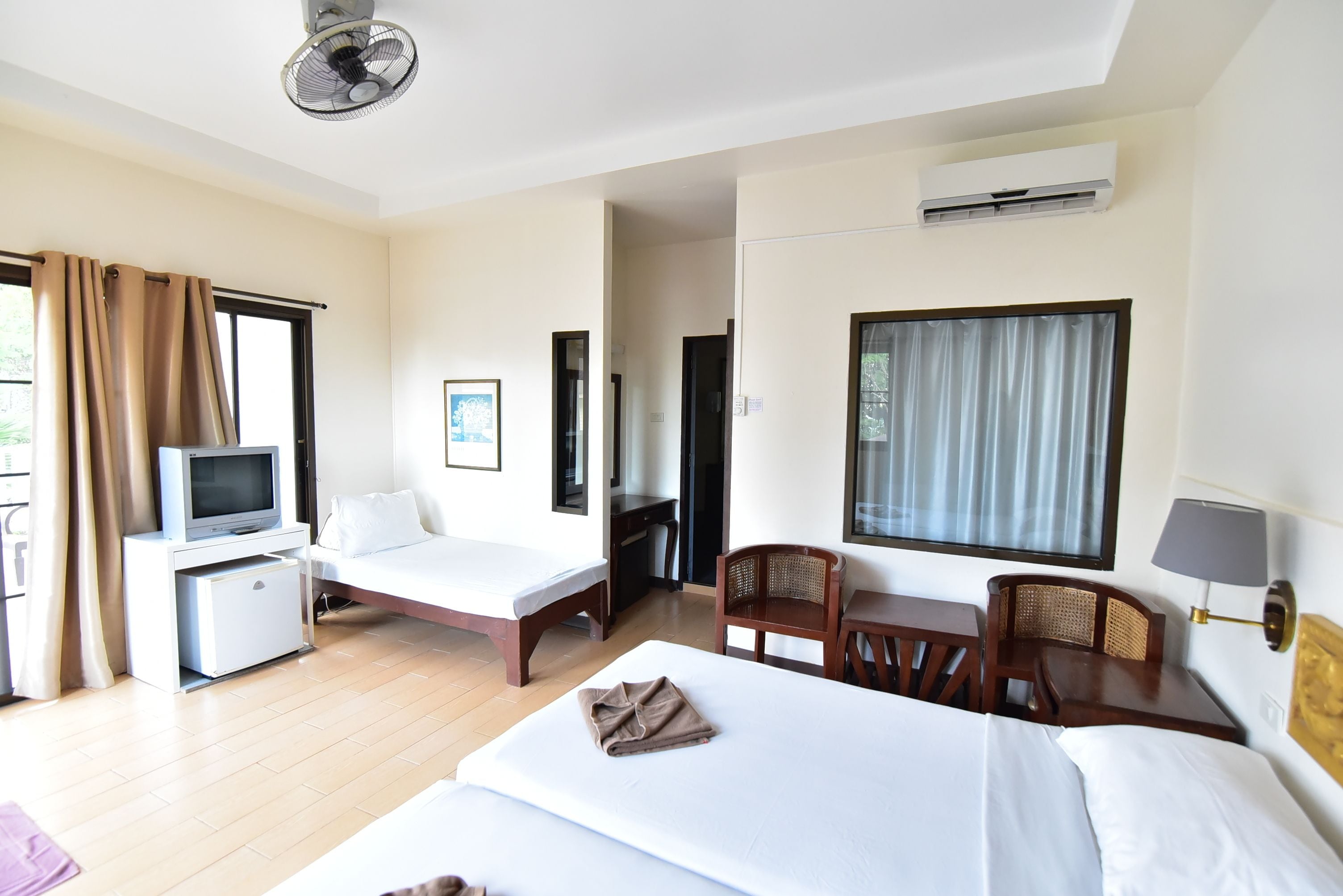 A hotel room with a bed, a desk, a chair, a TV, and an air conditioning unit.