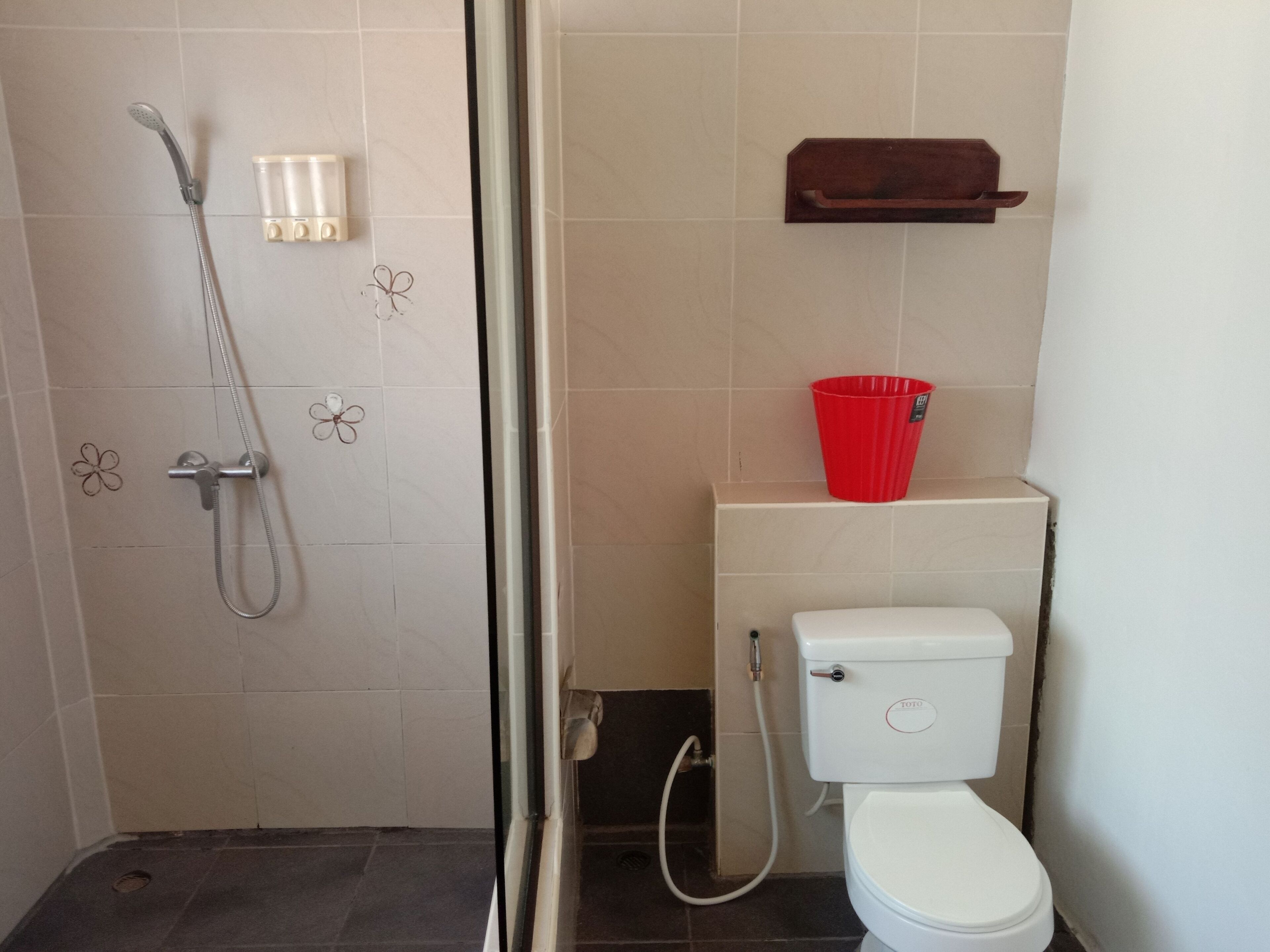 Un baño con ducha, inodoro y una cesta roja en la pared.