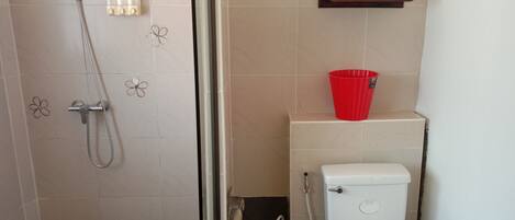 Un baño con ducha, inodoro y una cesta roja en la pared.