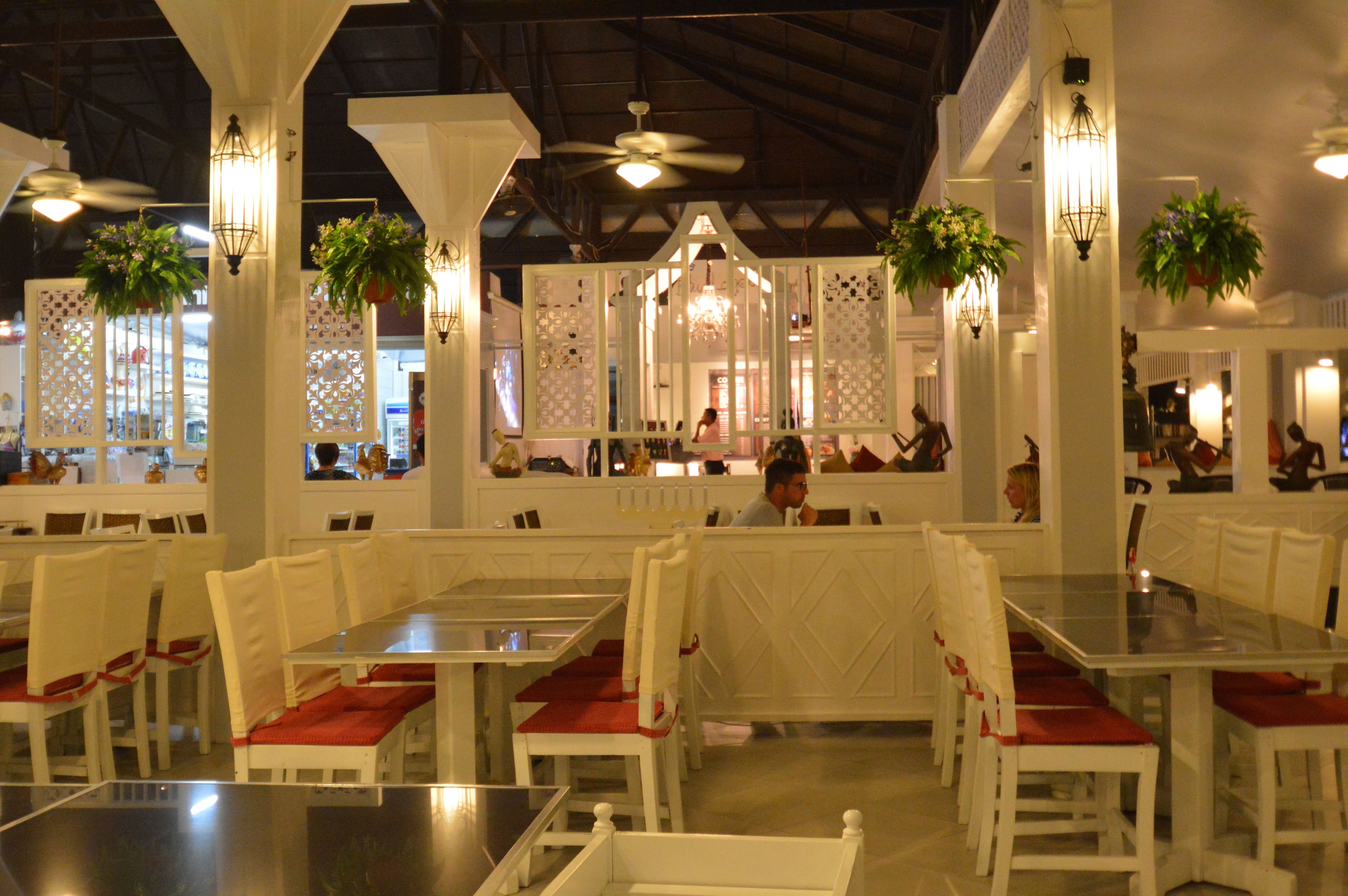 A restaurant with white tables and chairs, hanging plants, and a ceiling fan.