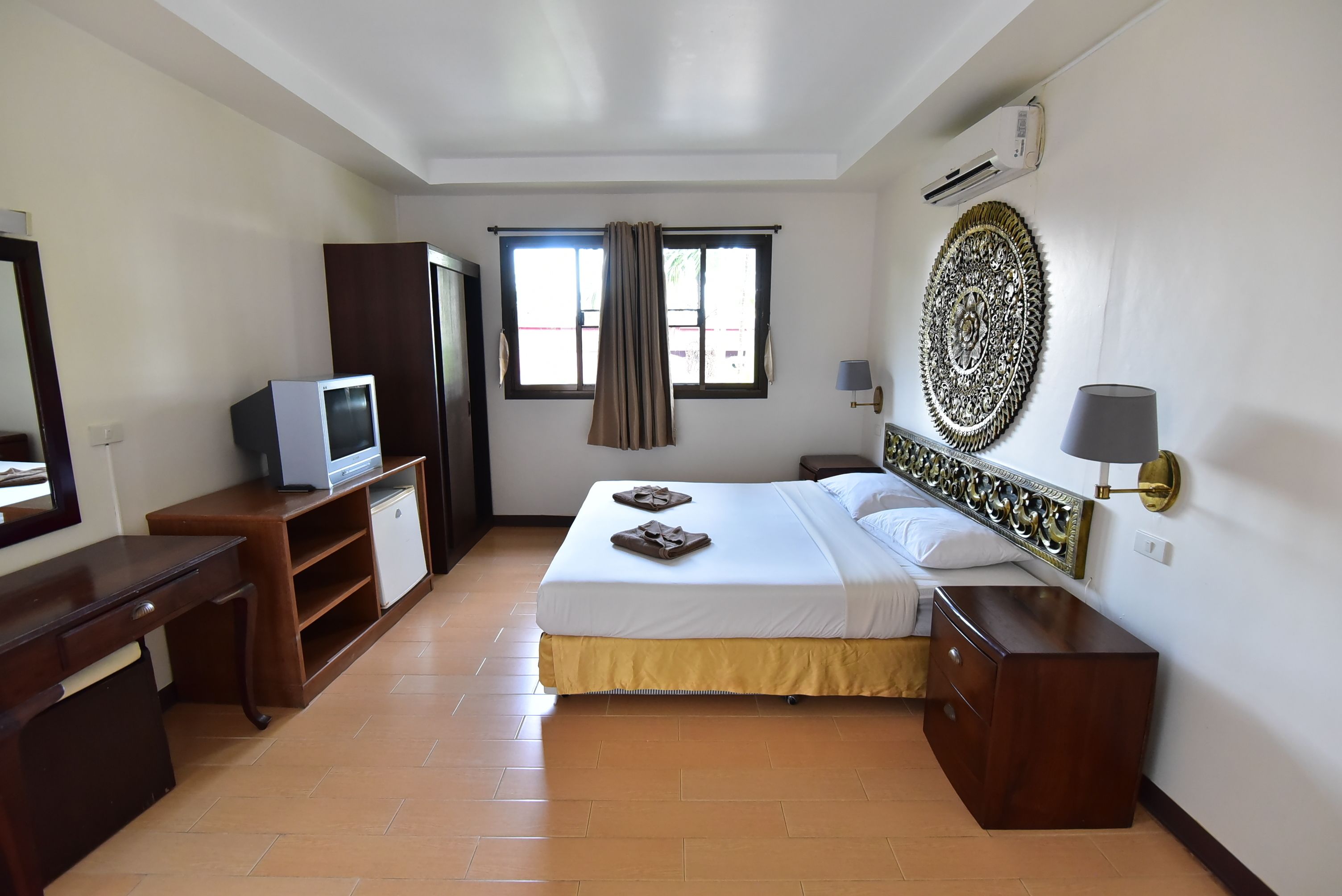 Une chambre d’hôtel comprenant un lit, un bureau, une télévision, une armoire, une fenêtre avec des rideaux et un élément décoratif mural.