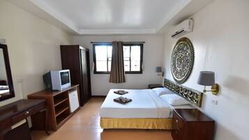 Habitación de hotel con cama, escritorio, televisor, armario, ventana con cortinas y un elemento decorativo en la pared.