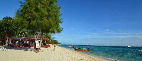 A beach with a wooden structure, a large tree, and boats in the water.