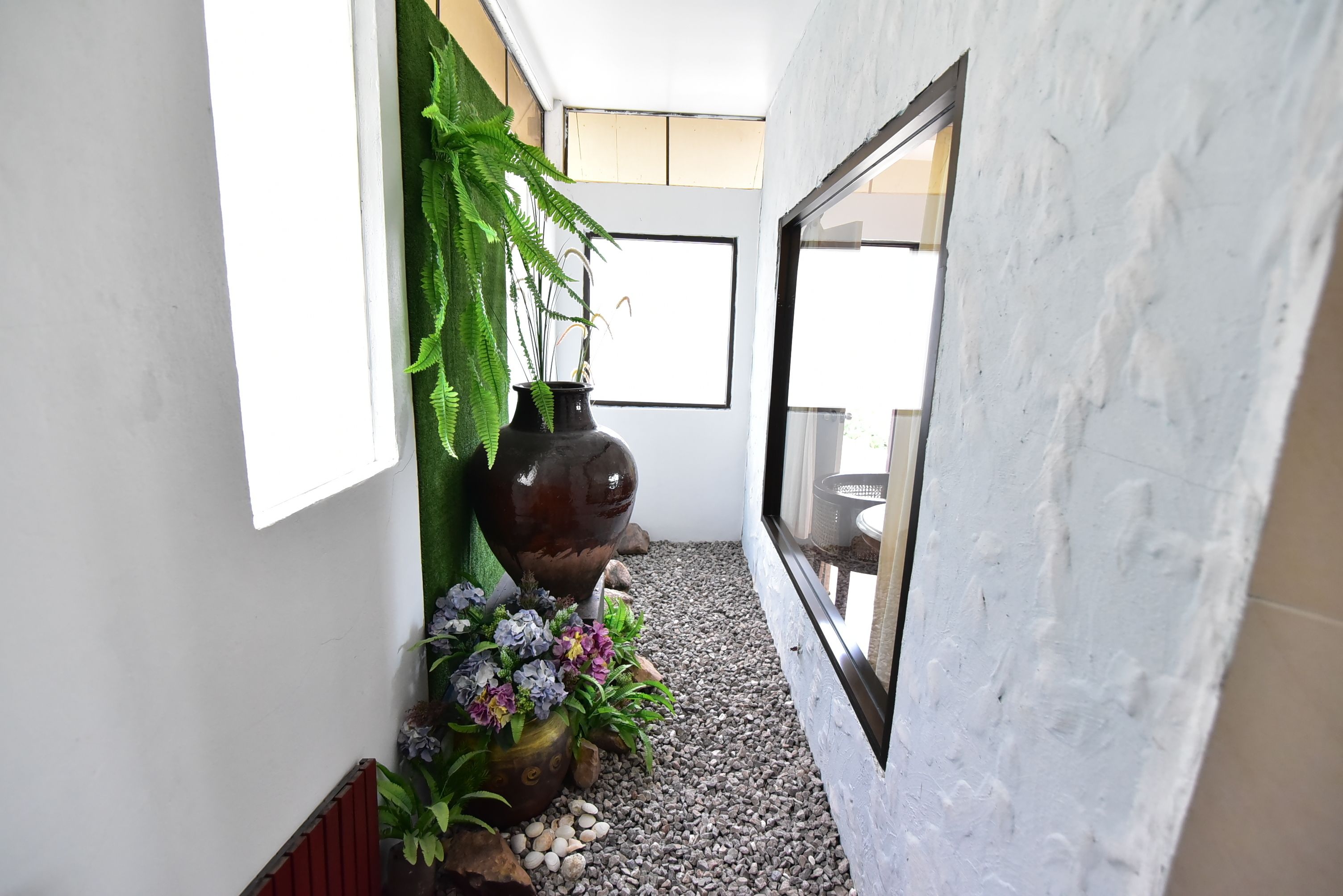 En gang med et stort vindue, en dekorativ vase med blomster og en sti belagt med sten.