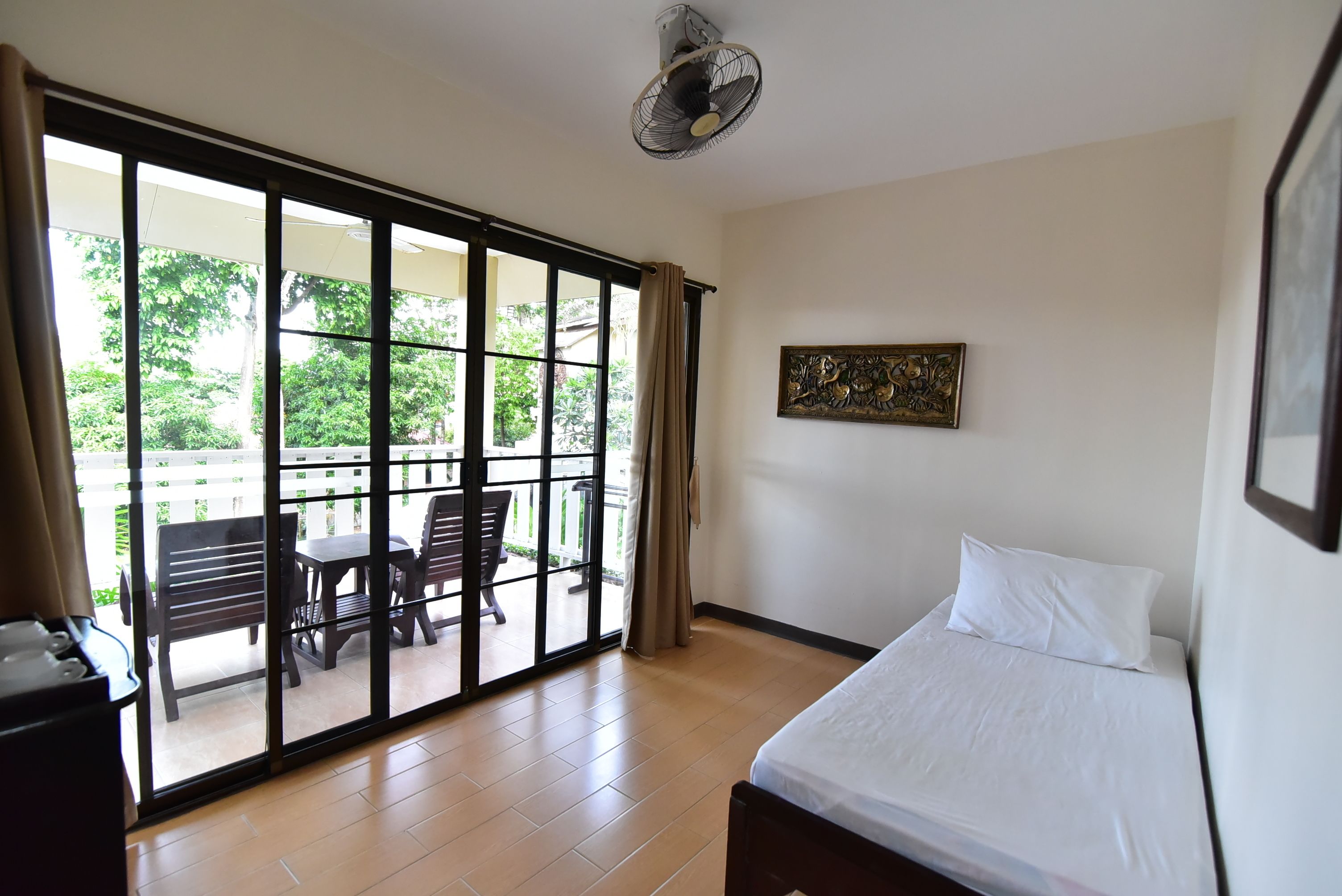 A hotel room with a bed, a ceiling fan, a sliding glass door leading to an outdoor seating area, and a framed artwork on the wall.