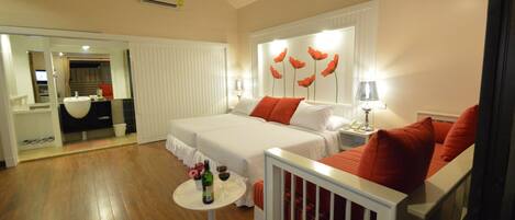 Habitación de hotel con dos camas, una mesita redonda con una botella y flores, y un espejo que refleja la habitación.