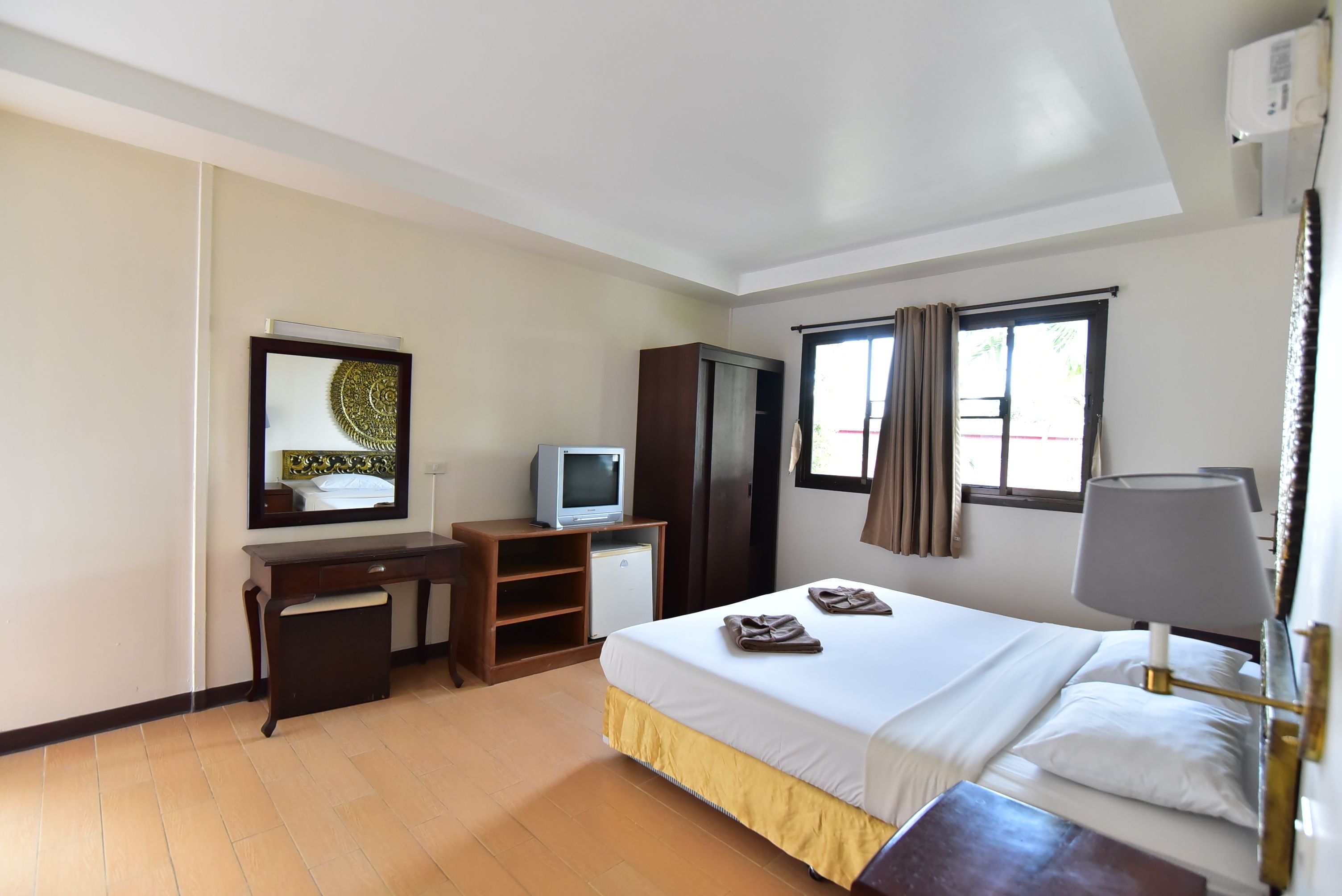 Una camera d'albergo con un letto, una scrivania con televisore, un armadio e una finestra con tende.